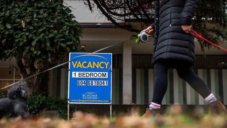 A dog-walker walks by a rental availability sign in Vancouver.