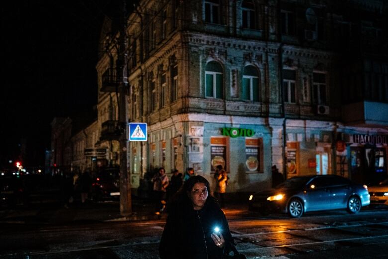 A woman holds a flashlight as she walks in a darkened street.