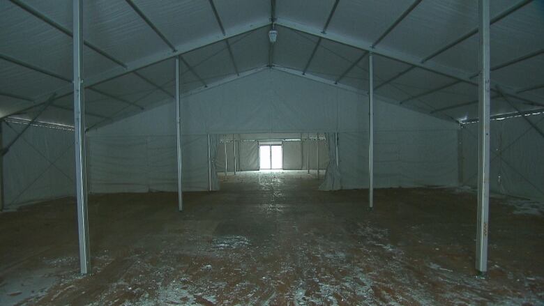 The interior of a large tent held up with metal poles with exit doors shown in the distance.