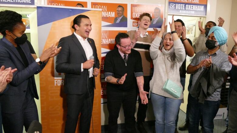 NDP leader Wab Kinew, MLAs Nahanni Fontaine and Uzoma Asagwara and NDP supporters cheer and clap alongside candidate Logan Oxenham.