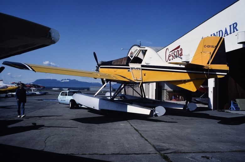 Yellow and white plane stands near an air hangar at YVR international airport. The plane was an agricultural plane mounted on floats for aerial firefighting. 