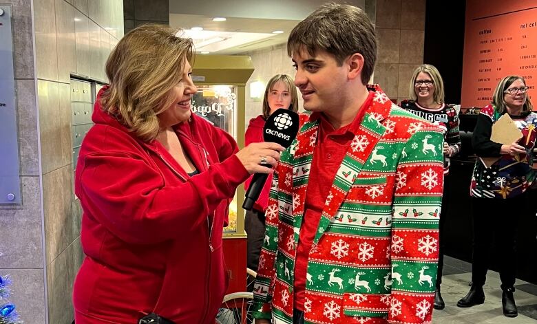 A woman holds a microphone in front of a man in a festive blazer.