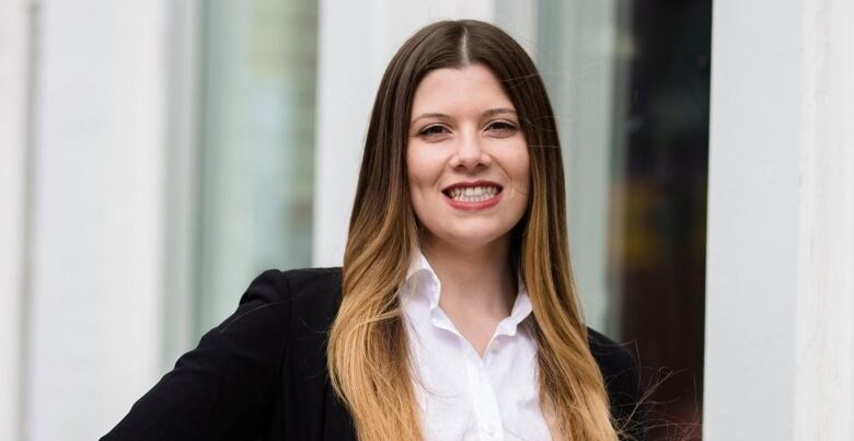 A woman in a white button-up blouse and a black blazer smiles at the camera.