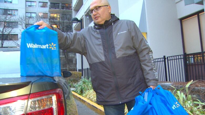 A man picks up his weekly grocery delivery from Walmart. His goods are packed in eight reusable bags. 