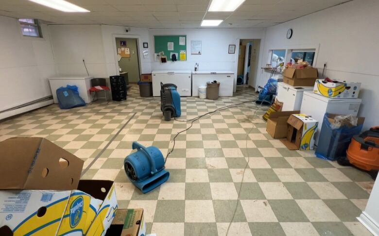 Large blue dryers are positioned in different spots on a basement floor that was recently flooded. 