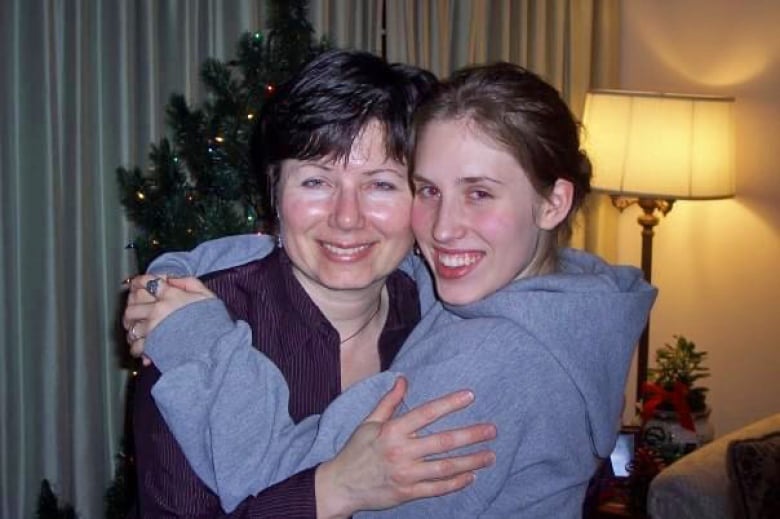 A younger woman hugs back another woman. 