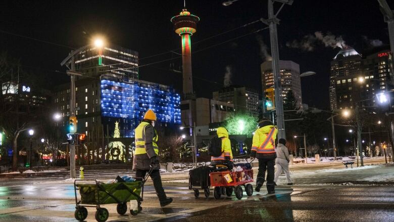 Three people wearing reflective vests walk through Calgary pulling carts full of supplies.