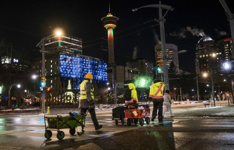 Three people wearing reflective vests walk through Calgary pulling carts full of supplies.