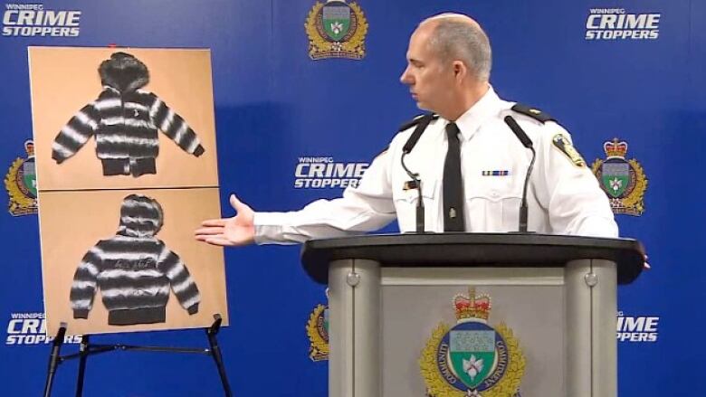 A man in a police inspector uniform gestures to his right at two photographs of a winter jacket