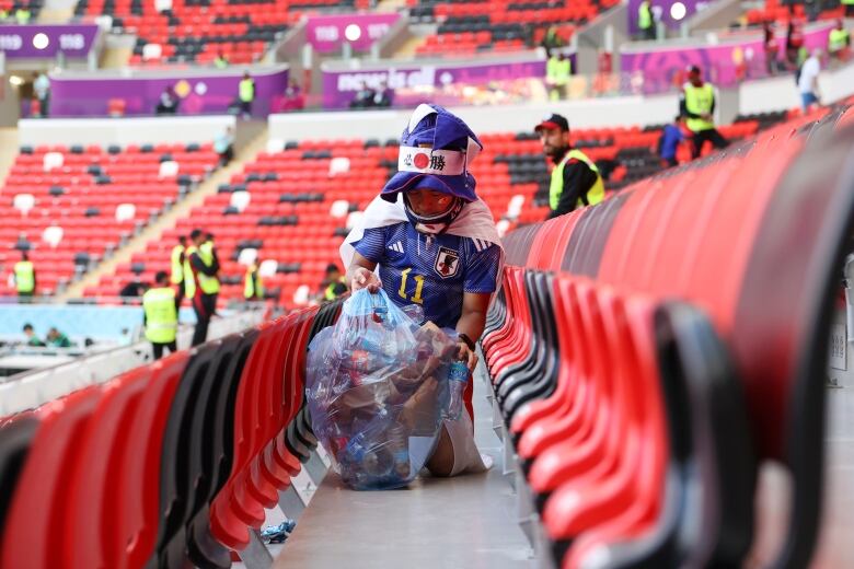 A woman picks up trash in soccer stadium.