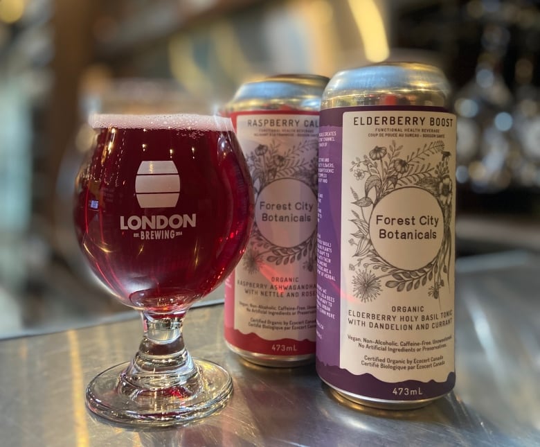 two cans of tonic with floral graphics sit beside a glass jar full of the drink on a bar counter