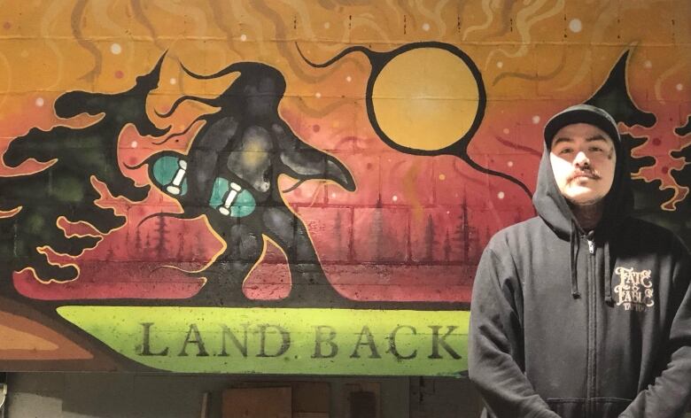 Man stands with mural. 