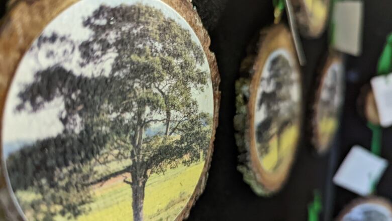 Round, wooden Christmas ornaments with a picture of a tree on them are hung on a black display board.