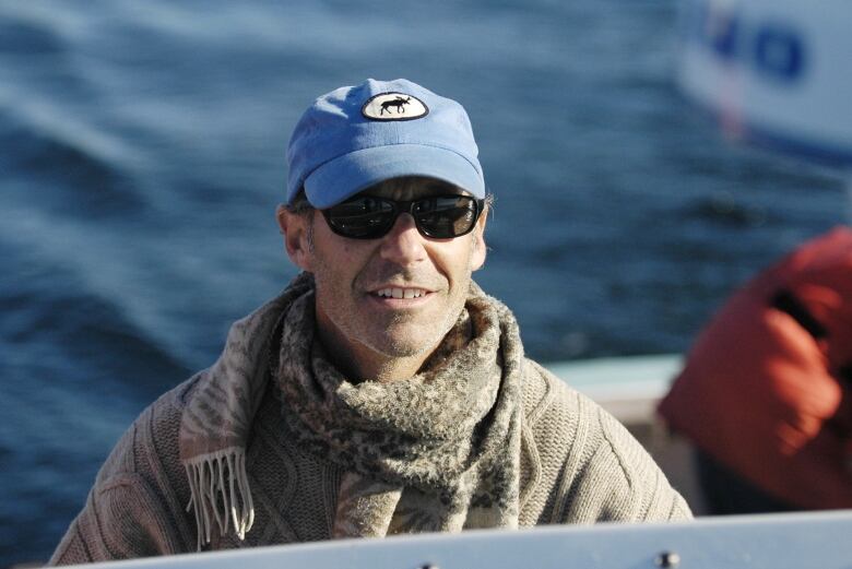 A man wearing a hat and sunglasses with water in the background