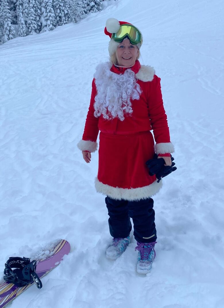 A woman in a Santa Claus outfit stands in snow at a ski resort.