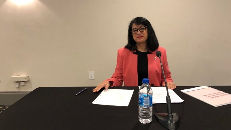 Manju Varma sits at a table with papers and a microphone in front of her.