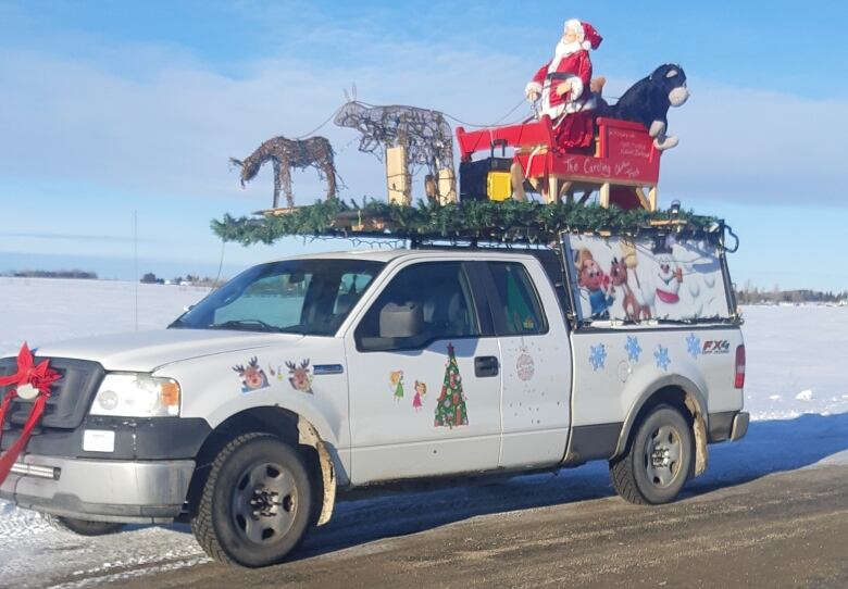 A white truck covered in holiday decorations sits on a snowy road.