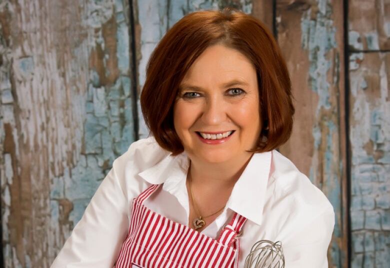 A woman in an apron smiles at the camera.