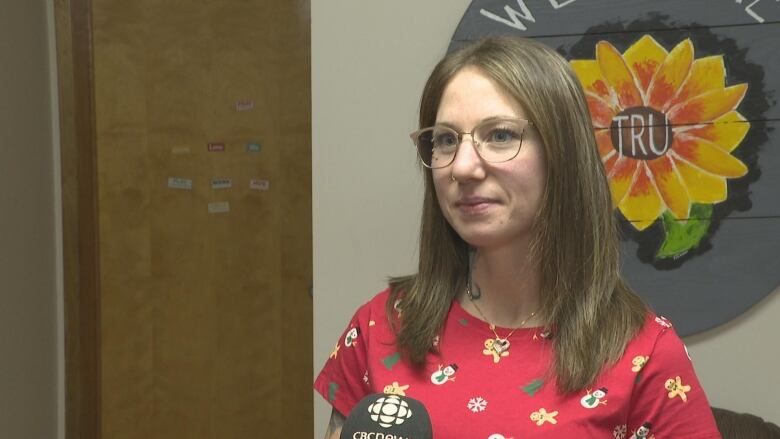 A woman in a red shirt with shoulder length hair speaks with a reporter during an interview.