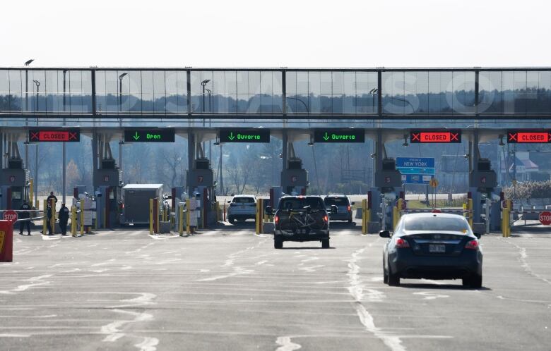 A road with cars leads to several border ports that have open or closed signs on them.