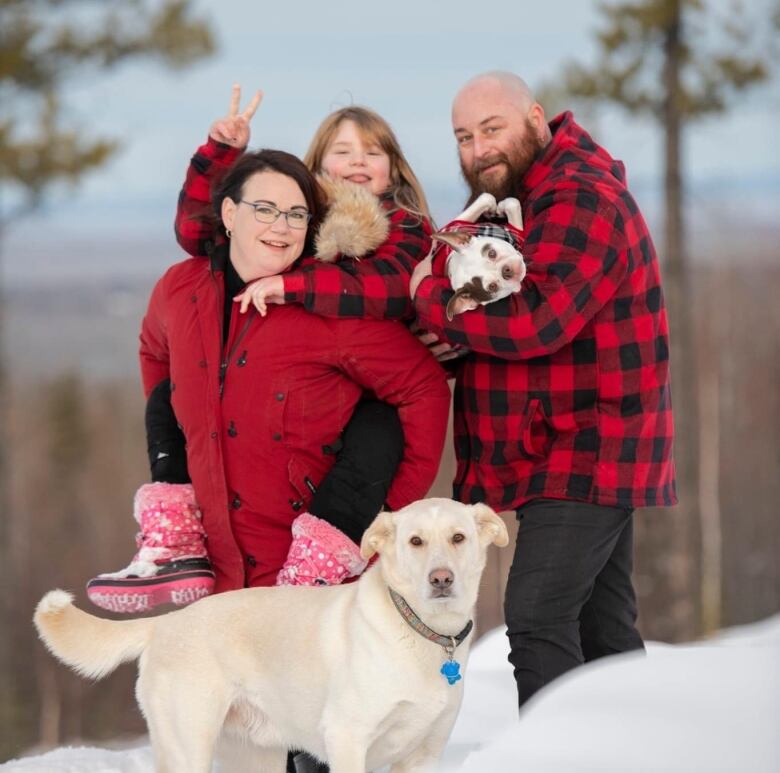 A family pose for a professional photo. Each family member is wearing a red flannel jacket, and a white retriever stands in the foreground.