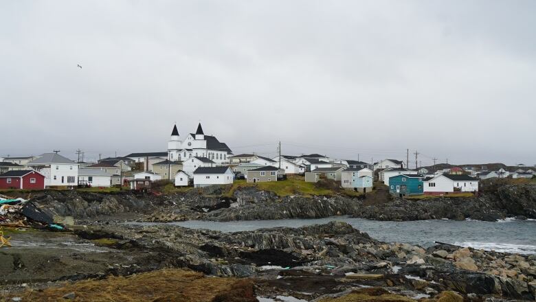 Various buildings, including a church, surround the ocean on a cloudy day. 