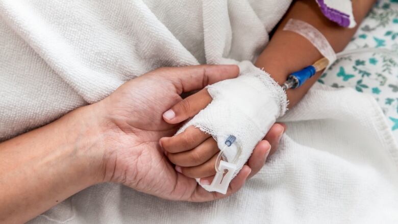 A mother holds a child's hand in the hospital. The child is connected to an IV