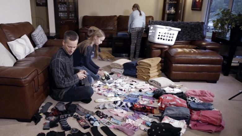 A father and three children sort and fold laundry spread out on a living room floor in front of them.