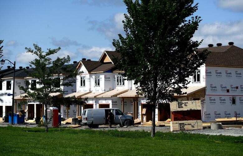 A row of unfinished houses and a light-coloured van are seen across a park.