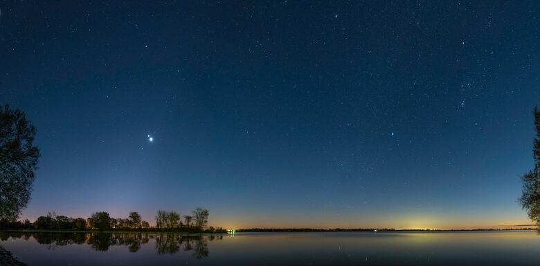 A starry sky, over a still lake shows two bright objects close together, which are Jupiter and Venus.