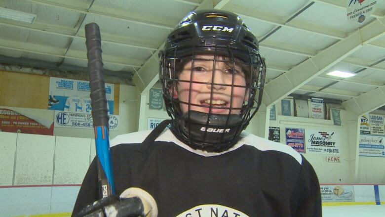 A pre-teen in hockey gear smiles and looks into the camera.