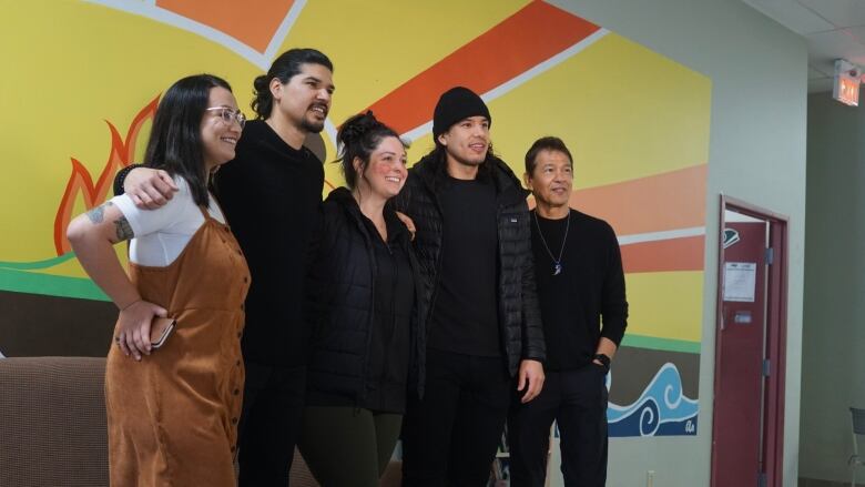 3 men and two women pose for a photo in front of a colourfully painted wall. 