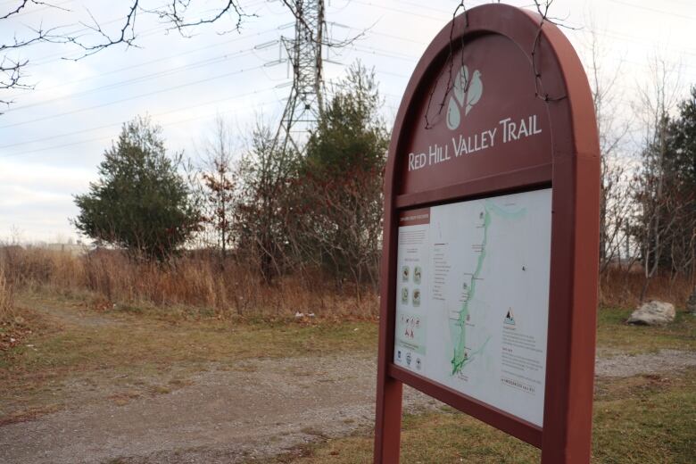 A photo of a trail map for the Red Hill Valley trail on Mount Albion. The sign is red metal and beside it is a hydro tower, which may be near the original dig. 