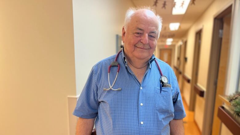 Doctor stands in a medical centre hallway, with his stethoscope around his neck. 