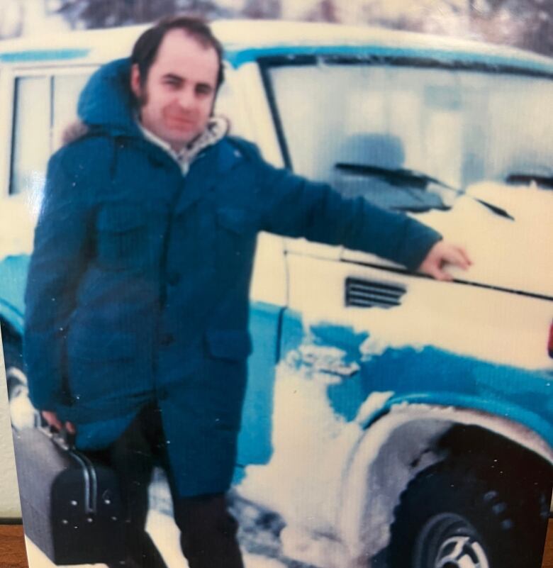 A scrapbook photo of the doctor, holding his medical bag, standing outside his blue truck covered in white snow on a cold winter day in PEI.