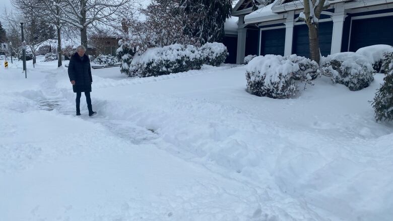 A woman walks along a narrow path carved by previous pedestrians in the snow where a sidewalk should be.