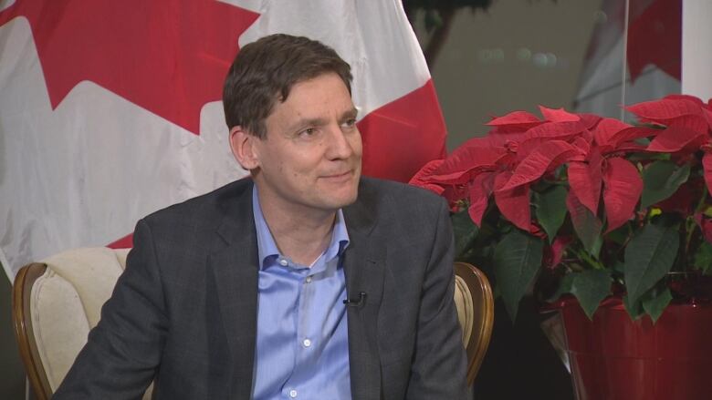 A man framed by the Canadian flag and poinsettias smiles for the camera.