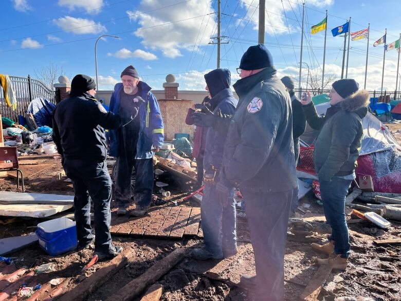 Police officers speak to a man wearing a blue coat and a tuque. Other men stand nearby. 