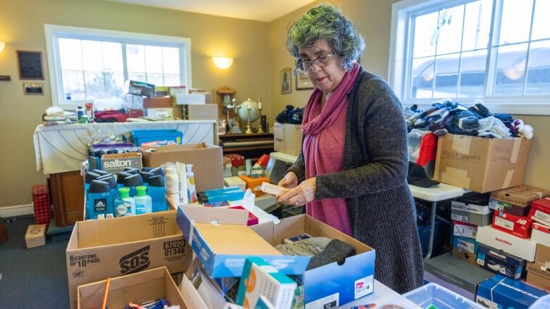 A woman stands by a table filled with shoeboxes that are being filled with necessities.