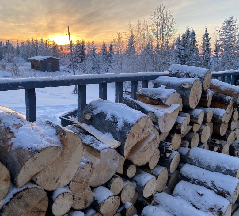 A stacked pile of wood on a porch with a sunset in the background.