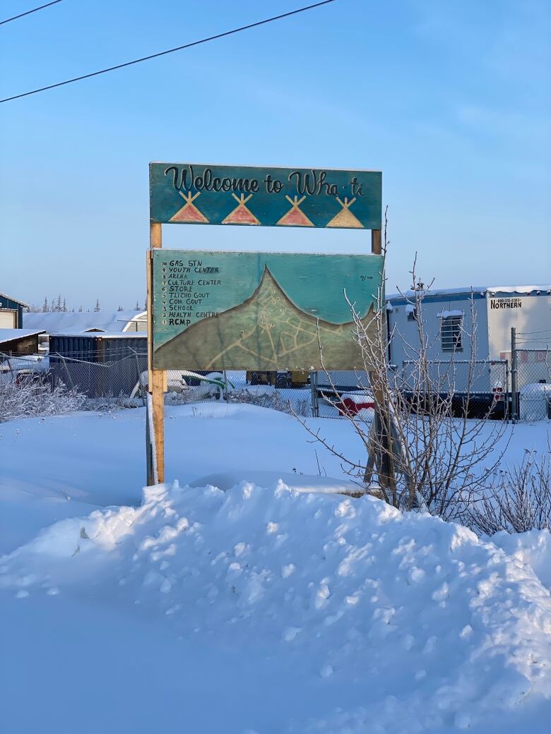 A wooden sign surrounded by snow with homes in the background.