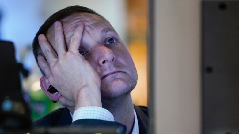 A man in a suit leans his face in his hands while looking at a screen