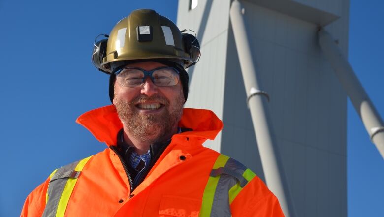 Steve Dunlop smiles for the camera wearing a hard hat, protective glasses and orange jacket. 