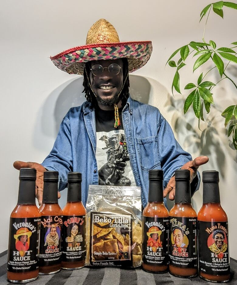 A man posing behind a table full of his hot sauces and chips.