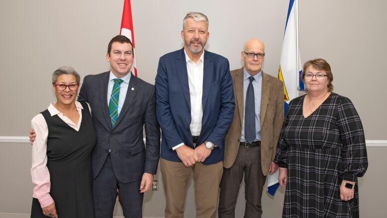 A group of five people - two women and three men - stand in a row in front of the Canadian and Nova Scotia flags.