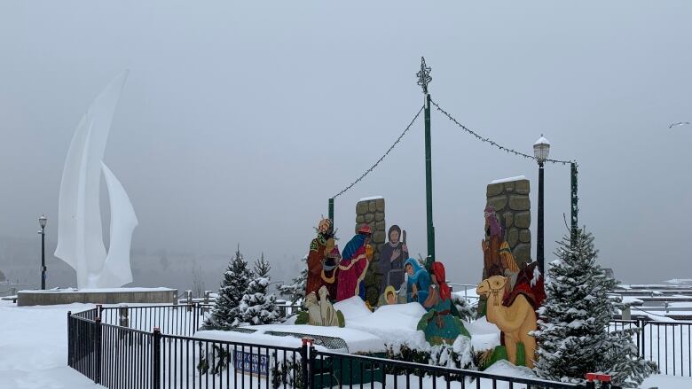 A nativity display near a statue in the shape of a sale, all covered with snow.