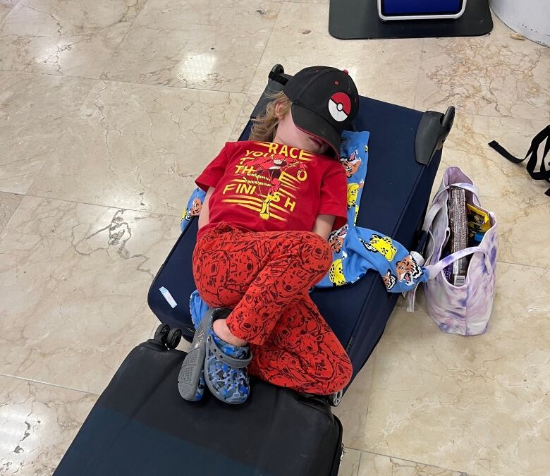 A small boy sleeps on bags of luggage, with his hat placed over his eyes. 