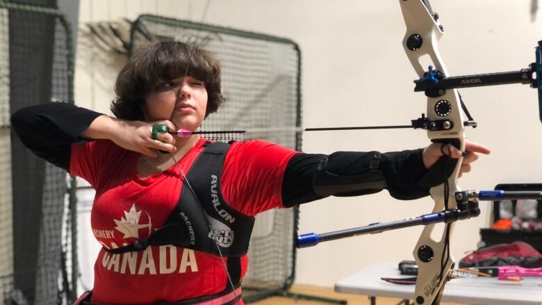 Young archer closes one eye and pulls her elbow back to aim her arrow. 