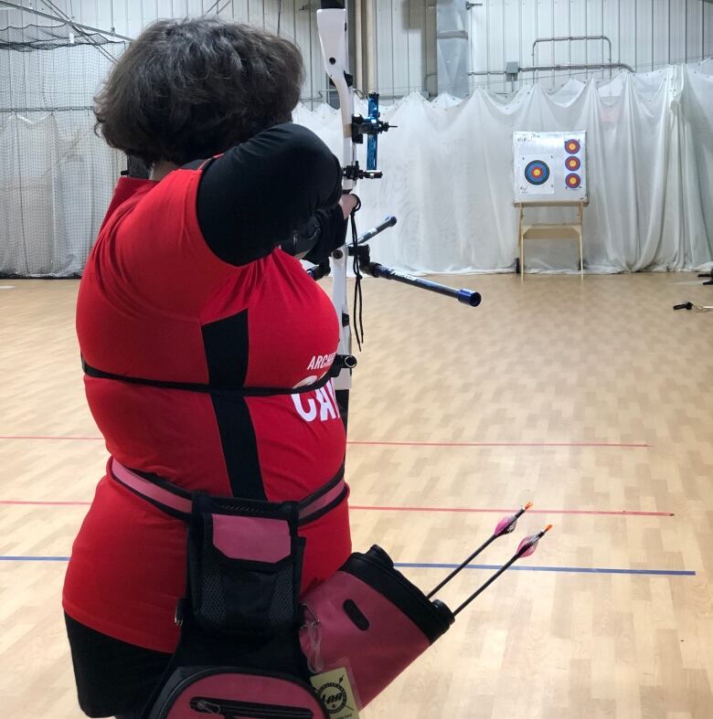 A young archer wearing an archery Canada T-shirt aims her arrow at the targets 18 meters away. 