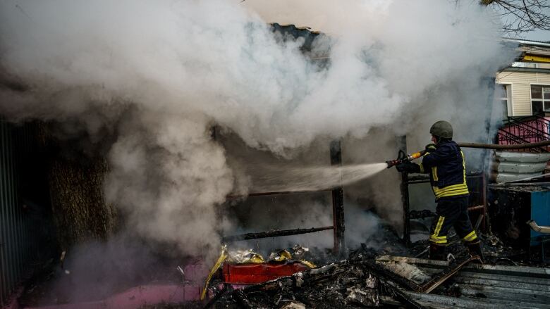 A firefighter directs a hose toward a burning building amid heavy smoke.